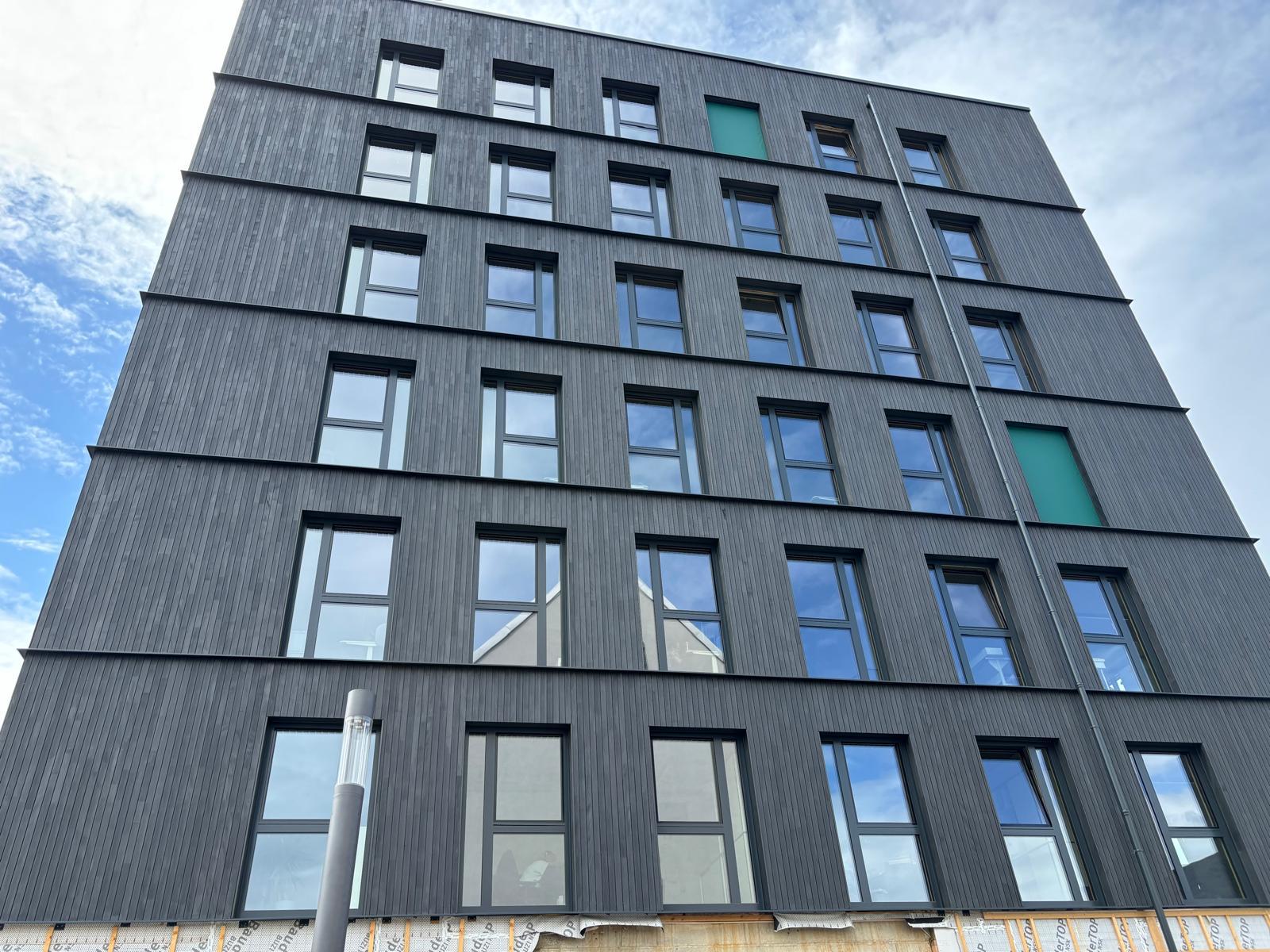Mehrgeschossiger Objektbau mit Holzfassade und Fensterreihen
